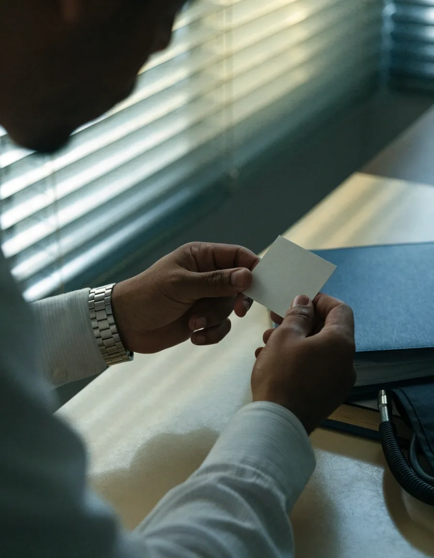 Hands holding a blank card over a plain desk in cool window light